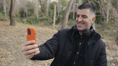 A-man-holds-his-phone-out-taking-selfies,-recording-stories-or-having-a-video-call-while-on-a-walk-in-the-forest