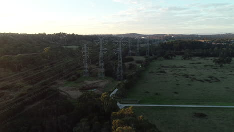 Aerial-approach-and-accent-beside-power-lines-crossing-green-belt-during-late-afternoon