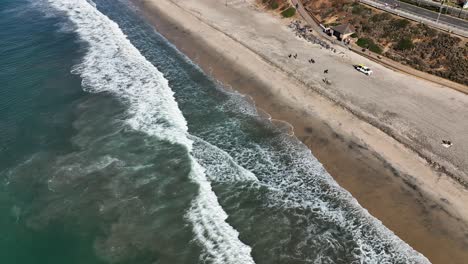 Tilt-up-video-of-waves-crashing-on-sandy-beach-along-the-coastline-and-the-beautiful-town-of-Carlsbad,-California,-USA