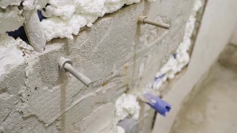 A-close-up-shot-of-an-aged-threaded-concrete-screw-and-plastic-plug-fixed-into-a-bathroom-wall,-tiles-have-been-removed-and-the-wall-left-bare-as-the-shower-undergoes-maintenance