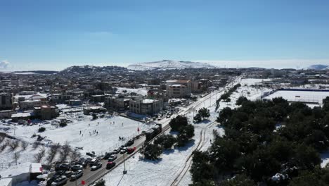 Green-trees-where-people-are-enjoying-the-winter-wonderland-while-a-truck-is-driving-over-the-main-road-with-snow-in-the-trailer-in-Buqata-Israel