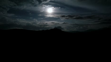 Hyperlapse-of-full-moon-at-a-cloudy-night-with-dark-silhouette-of-mountains