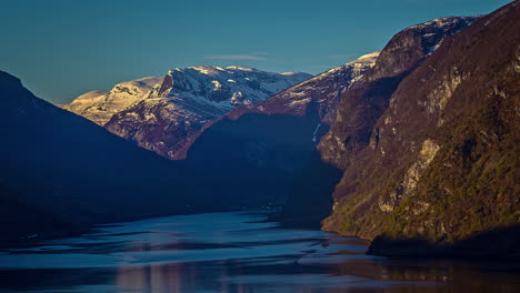 Beautiful-tranquil-Fjord-Water-surrounded-by-snowy-mountains-lighting-by-sunrise-in-Norway---Timelapse-wide-shot
