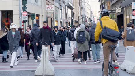 A-diverse-crowd-of-men-and-women-use-a-city-crosswalk-in-a-downtown-shopping-district,-slow-motion