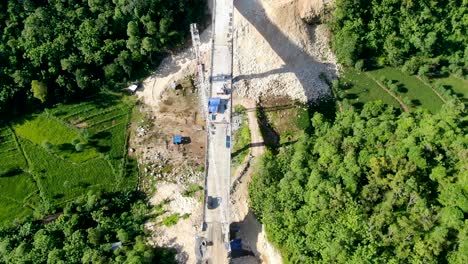 Workers-building-bridge-over-valley-in-forestry-landscape,-aerial-drone-view
