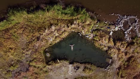 aerial-view-of-a-woman-floating-treading-water-in-a-black-bikini-enjoying-the-pure-serenity-of-an-outside-thermal-hot-spring-in-eastern-oregon