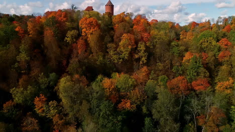 Ascending-aerial-shot-of-colorful-trees-and-Turaida-Castle-on-hilltop-during-sunny-autumn-day-in-Latvia,Europe