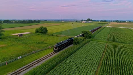 An-Aerial-View-of-a-Steam-Train-Approaching-Flying-Ahead-Traveling-Thru-Farmlands-and-Corn-Fields-Blowing-Smoke-on-a-Sunny-Summer-Day
