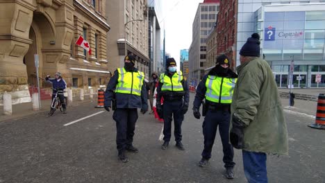 Man-holding-a-megaphone-speaking-with-police-officers-while-protesters-with-canadian-flags-walk-during-the-Freedom-convoy