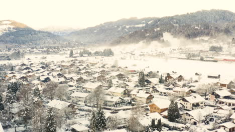 Snowy-town-of-Garmisch-Partenkirchen-below-mountains,-drone-shot
