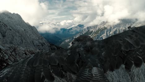 Close-aerial-of-a-falcon-bird-flying-over-the-panoramic-alp-mountain-range-scenary-with-the-sky-full-of-clouds