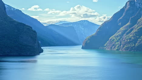 Zeitrafferaufnahme-Von-Fliegenden-Weißen-Wolken-Zwischen-Norwegischen-Bergen-Und-Einem-Kreuzfahrtschiff,-Das-Den-Fjord-An-Einem-Sonnigen-Tag-Verlässt