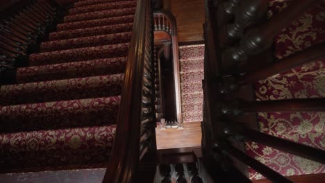 Looking-down-an-old-staircase-in-a-1900's-mansion-with-red-carpet-steps