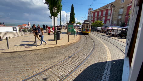 Slow-motion-shot-during-drive-with-famous-tramway-in-Lisbon-during-sunny-day,-tourist-and-people-walking-on-promenade-of-city