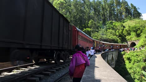 Statische-Aufnahme-Eines-Langen-Zuges-Mit-Vielen-Waggons,-Die-Aus-Einem-Tiefen-Bergtunnel-Herauskommen,-Menschen,-Die-Auf-Der-Brücke-Mit-Neun-Bögen,-Sri-Lanka,-Beiseite-Schauen