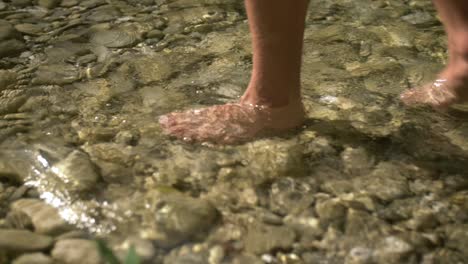 man-walking-barefoot-in-pure-cold-clear-river,-slow-motion-closeup