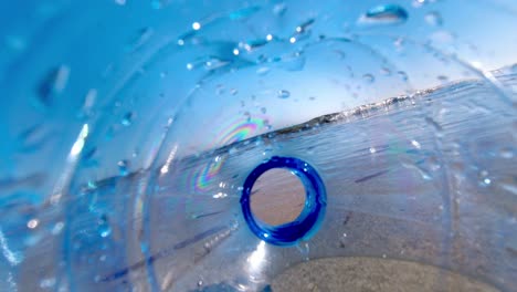 Plastic-bottle-discarded-on-the-beach-carelessly-is-swept-out-to-see-by-the-waves-and-tide---as-seen-from-inside-the-bottle