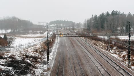 Aerial-shot-of-a-speed-train,-Arlanda-Express-passing-by-under-drone-in-industrial,-winter-landscape-going-towards-Stockholm-City-Terminal