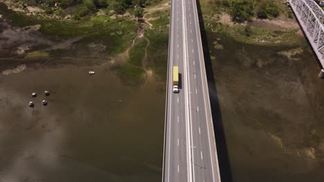 Aerial-tracking-shot-of-yellow-truck-driving-on-Barra-de-Santa-Lucia-Bridge-during-sunny-day-in-Uruguay