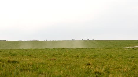 Dust-of-a-dirt-road-being-blown-away-over-the-green-meadows-of-the-European-countryside