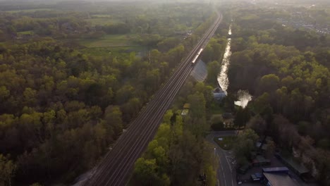 Beautiful-aerial-view-of-train-travelling-at-sunset-with-forest-and-fields