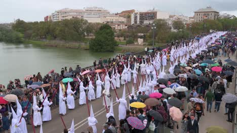 Penitents-march-during-a-procession-crossing-the-Triana-bridge-in-celebration-of-the-Holy-Week-in-Seville,-Spain