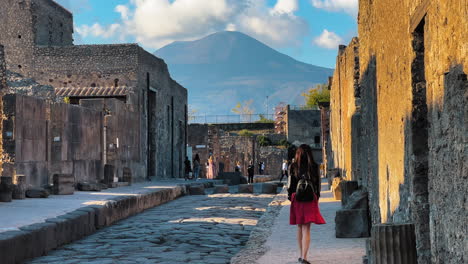 Slow-motion-shot-of-female-person-walking-between-old-walls-of-Pompeii-in-Italy---Giant-Volcano-surrounded-by-clouds-in-backdrop