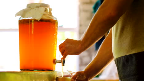 Caucasian-man-pours-brewed-kombucha-from-container,-probiotic-drink