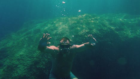 Man-with-arms-wide-open-snorkeling-and-swimming-underwater-in-apnea-with-diving-mask-in-turquoise-crystalline-sea-water