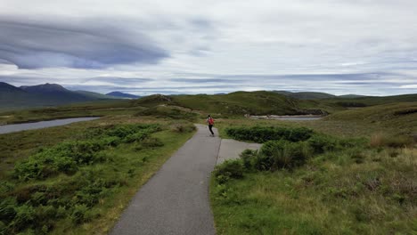 Aerial-Following-Carefree-Male-Longboarding-Along-Empty-Path-In-North-West-Scotland