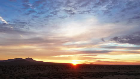 Golden-Leuchtender-Sonnenuntergang-In-Der-Mojave-Wüste-Mit-Einem-Bemerkenswert-Farbenfrohen-Himmel-über-Der-Zerklüfteten,-Trockenen-Landschaft