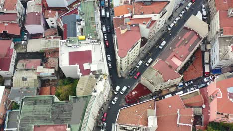 Aerial-top-down-view-of-cars-at-a-fork-in-the-road-surrounded-by-old-and-tall-European-residential-buildings-with-orange-roofs-on-a-cloudy-day-in-Istanbul-Turkey