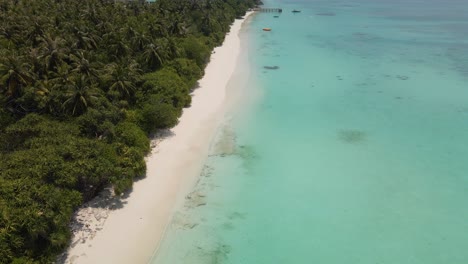 Drohnenflug-über-Der-Küste-Der-Maledivischen-Insel,-Blaues-Wasser-Vor-Einem-Wunderschönen-Himmel-Und-Ein-Pier-Im-Wasser