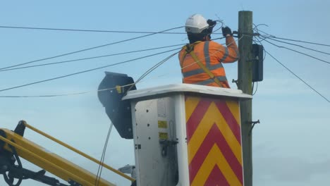 Telecom-technician-working-on-repairing-telephone-pole-power-cable-in-boom-crane-basket