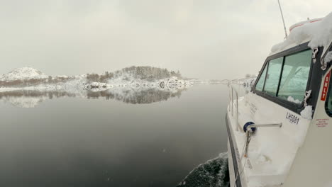 view-along-the-cockpit-of-a-boat-as-it-cruises-through-incredibly-calm-water-with-snow,-sun-and-snow-covered-hills-of-Norway