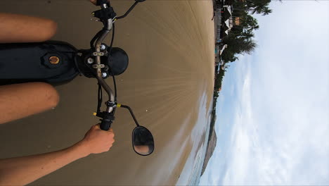 Person-riding-motorbike-on-sandy-beach-of-Vietnam,-vertical-POV-shot
