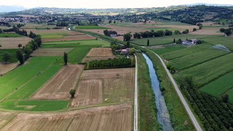 Aerial-shot-of-a-wide-field-in-Italy,-following-a-river