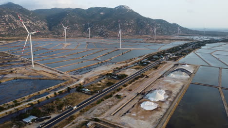 Aerial-panoramic-view-of-wide-salt-fields-and-wind-turbines,-with-a-road-crossing