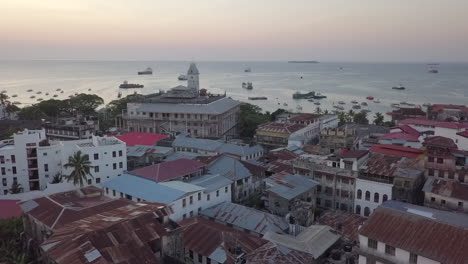Sunset-aerial-pans-over-Stone-Town,-Zanzibar-waterfront,-moored-boats