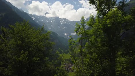 Luftwagen-Zwischen-Büschen,-Die-Ein-Malerisches-Grünes-Tal-Und-Ein-Kleines-Dorf,-Umgeben-Von-Bergen-Und-Wald,-Schweizer-Alpen,-Enthüllen