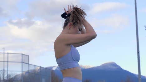 Young-Asian-woman-in-sports-bra-putting-hair-in-bun-with-scrunchie-tie,-Profile