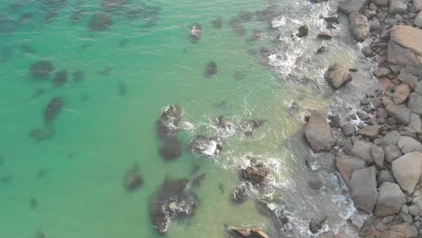 Luftbild-über-Seichtes-Wasser,-Das-Am-Strand-Von-Jiwani-In-Die-Felsige-Küste-Stürzt