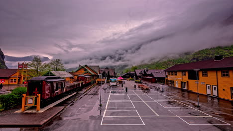 Timelapse-shot-of-train-waiting-in-the-railway-station-in-Norwegian-Fjord-in-Flam,-Norway-on-a-cloudy-day-with-dark-clouds-covering-the-mountain-peaks-in-timelapse