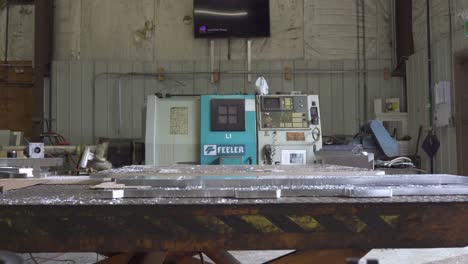 Mann-Geht-Durch-Werkstatt-Mit-Aluminiumplatten-Auf-Tisch-Und-Drehmaschine-Im-Hintergrund