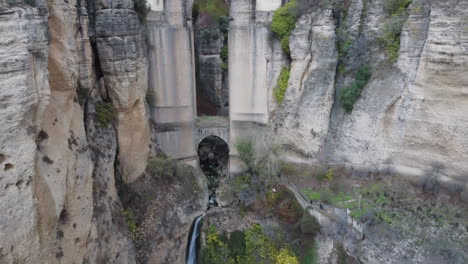 Aerial-descends-height-of-historic-arch-bridge-over-deep-chasm,-Spain