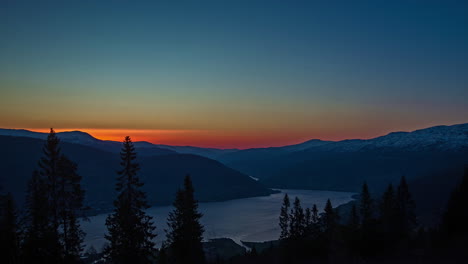 Time-lapse-shot-of-golden-sunrise-behind-mountain-range-and-tranquil-fjord-water-in-the-valley