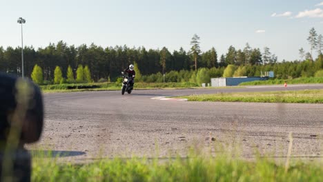 Biker-on-motorbike-riding-turn-on-forest-race-track,-then-wave-by-hand