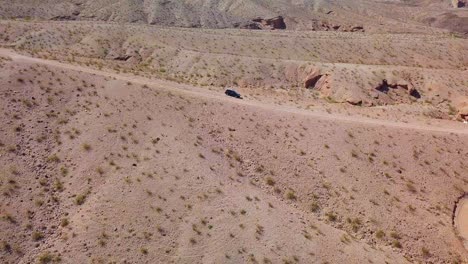 Aerial-view-away-from-a-car-parked-on-a-desert-dirt-road,-in-sunny-Kingman-wash,-USA---pull-back,-drone-shot
