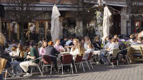 Happy-students-meet-and-drink-in-a-sunny-terrace-cafe-at-Oude-Markt---Concept-of-college,-party,-people,-fun---Leuven,-Belgium
