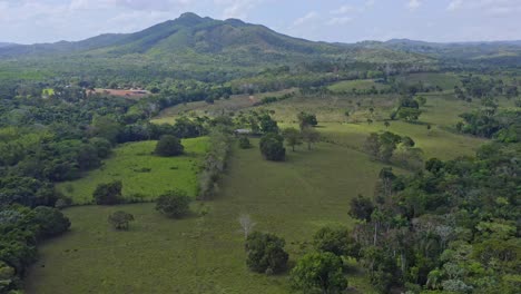 Aerial-backwards-shot-of-exotic-nature-landscape-of-Bayaguana-during-sunlight---Growing-plants-,bush-and-trees---Green-Mountains-in-backdrop